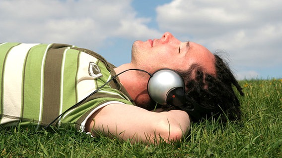 Ein junger Mann mit Kopfhörern liegt im Gras und hört Musik. © Edyta Pawlowska - Fotolia 